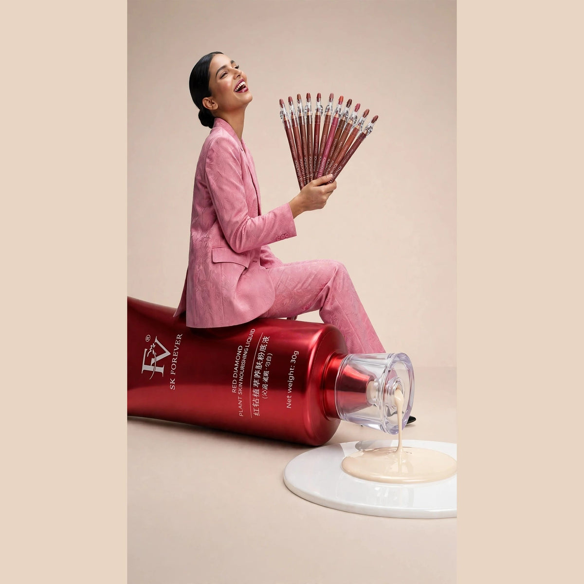 Young woman in pink suit sitting on giant FV Red Diamond foundation tube holding fanned bouquet of 12 giant Flormar matte lip liners with clear sharpener caps - ivory foundation drip on glossy white platform - flawless base combo concept
